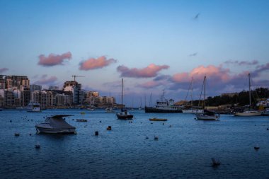 Valetta, Malta - 18 Nisan 2023 Sliema Körfezi 'nde gün batımı. Sudaki küçük tekneler, arka plandaki oteller, gökteki pembe bulutlar.. 