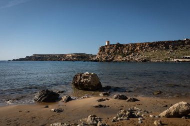 Malta, Golden Beach 'teki Akdeniz sahili manzarası. Mavi su, ön planda kumdaki kayalar.. 