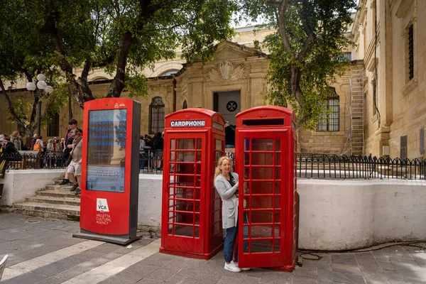 stock image Valetta, Malta - April 19, 2023: Woman posing for photo between two British red telephone boxes in historical old town. 