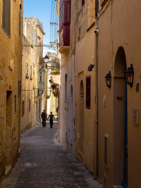 Rabat, Gozo, Malta - 18 Nisan 2023: Dar bir sokakta tarihi mimariyle yürüyen bir çift. 
