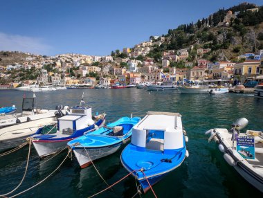 Symi, Yunanistan - 30 Mayıs 2023: Yunanistan 'ın Symi adasının deniz kıyısındaki renkli mimari. Ön planda küçük mavi botlar. 