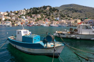 Symi, Yunanistan - 30 Mayıs 2023: Yunanistan 'ın Symi adasının deniz kıyısındaki renkli mimari. Ön planda küçük mavi botlar. 