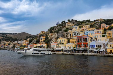 Symi, Yunanistan - 30 Mayıs 2023: Yunanistan 'ın Symi adasının deniz kıyısındaki renkli mimari. İskeleye demirlemiş motorlu tekne.. 