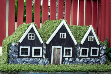 Three small black wooden elf houses with green moss roof, typical for Iceland. clipart