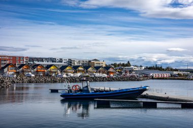 Reykjavik, İzlanda - 25 Eylül 2023: Karsnes limanında demirli mavi sandal, Kopavogur. Arka planda kıyı şeridi boyunca renkli kulübeler. 