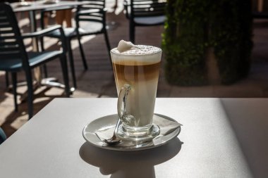 Caddedeki bir kafede masanın üzerinde duran uzun bardakta sütlü kahve. Bulanık arkaplan, insan yok. 