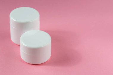 İki beyaz kozmetik kavanozu pembe arka planda duruyor. Kozmetoloji, tıp, güzellik, sağlık ve bakım