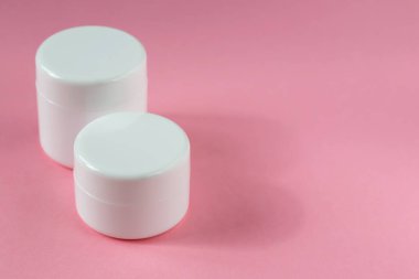 Two white cosmetic jars are standing on a pink background. Cosmetology, medicine, beauty, health and care clipart