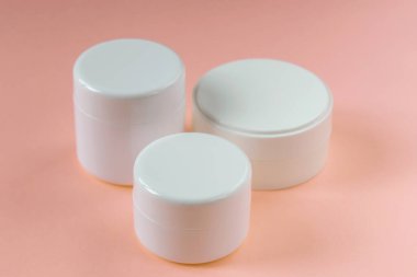 Üç kozmetik kavanozu pembe arka planda duruyor. Kozmetoloji, tıp, güzellik, sağlık ve bakım