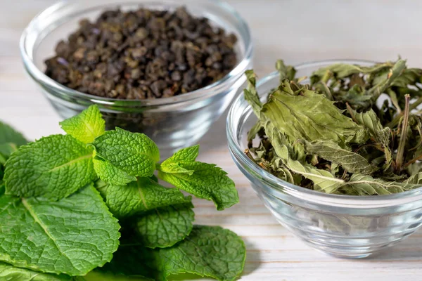 Fragrant dried mint and green tea in a glass bowl. Near it sprigs of fresh mint. Benefits and health. Close-up