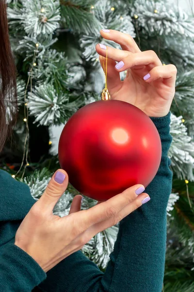 Women\'s well-groomed hands with manicure hang a red ball on the Christmas tree. New year, Christmas. Hand care