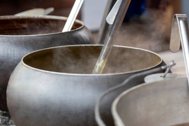 Arka arkaya birkaç büyük tencere ve sıcak yemek standı. Buhar onlardan geliyor. Yemek katı. Sokak yemeği.