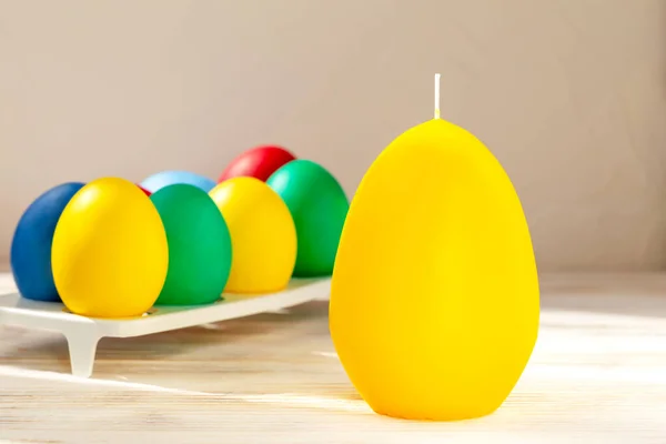 Easter. A large yellow egg-shaped candle stands on the table. Behind it in a stand are Easter eggs