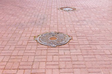 Two iron hatches on the ground in the middle of tiles with fallen dry leaves