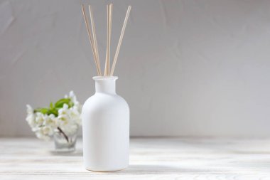 Perfume for home. Aromatic reed diffuser with sticks and flowers in a vase on a white wooden background. The concept of tranquility, relaxation and enjoyment