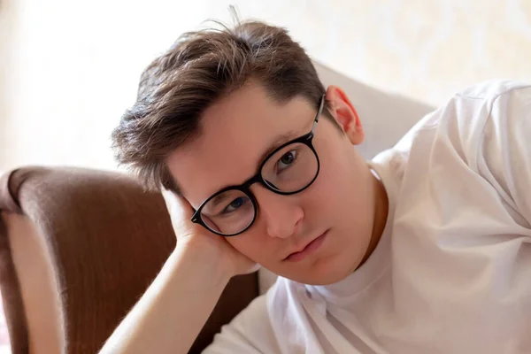 A young guy with glasses is lying on the couch, leaning on his arm and looking attentively