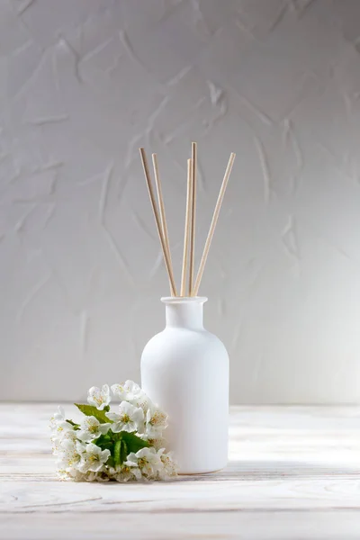 Perfume for the home. Aromatic reed diffuser and flowers in on a white background. The concept of tranquility, relaxation and enjoyment. Vertically