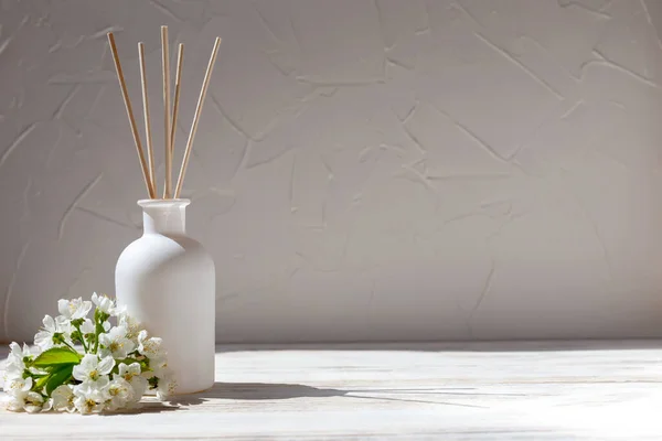Perfume for home. Aromatic reed diffuser with sticks and flowers on a white wooden background in sunlight. The concept of tranquility, relaxation and enjoyment