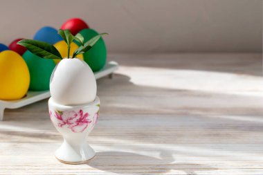 Easter. In the stand is an egg from which a sprout grows on a wooden background. Behind it in the tray are Easter eggs. The concept of new life