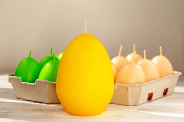 Easter. A large yellow egg-shaped candle stands on the table. Behind it are green and beige egg-shaped candles in trays