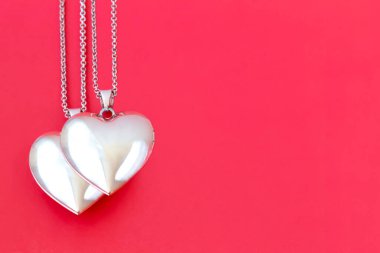 Two pendants on a chain in the form of a heart on a red background. Valentine's Day. Flat lay, copy space
