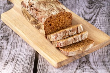 Loaf of freshly baked dark bread on a board with cut pieces on a wooden background. Close-up