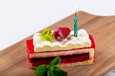 Fresh delicious beautiful raspberry cake with berry, mint leaves and burning candle on wooden board