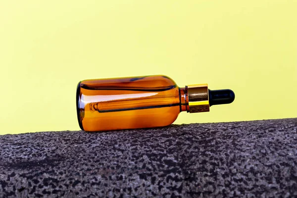 Glass cosmetic amber bottle lying on bark tree on yellow background. Organic cosmetics. Natural care