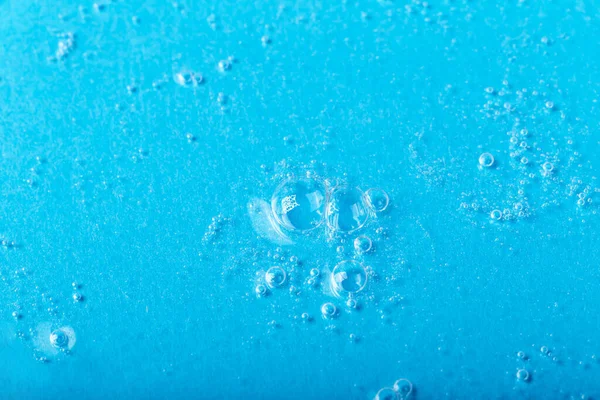 Textured background of transparent liquid with bubbles on blue background. Cosmetics, gel, transparent texture, lotion. Selective focus, defocus