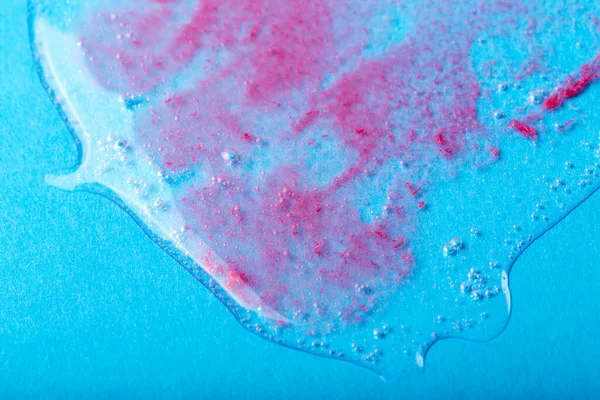 Transparent liquid with red particles on blue background. Laboratory studies. Cosmetics, gel, transparent texture, lotion. Selective focus, defocus