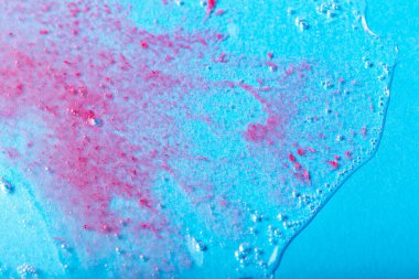 Mavi zemin üzerinde kırmızı parçacıklar olan kabarcıklı şeffaf bir sıvı. Laboratuvar çalışmaları. Kozmetik, jöle, şeffaf doku, losyon. Seçmeli odak, ayrışma