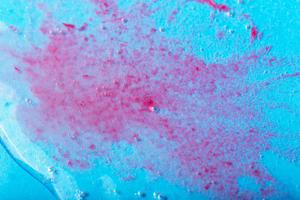 Red particles in transparent liquid with bubbles on blue background. Laboratory studies. Cosmetics, gel, transparent texture, lotion. Selective focus, defocus