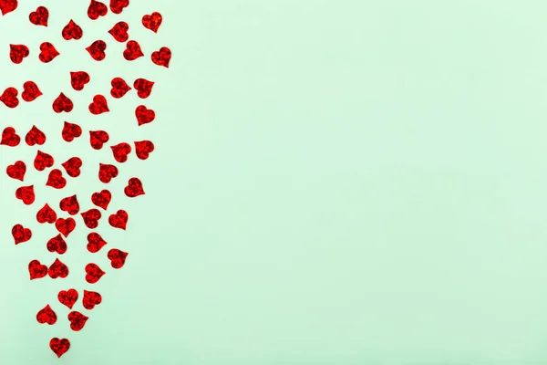 Small red hearts on light green background with copy space. Valentine\'s Day. Concept of love, care and tenderness