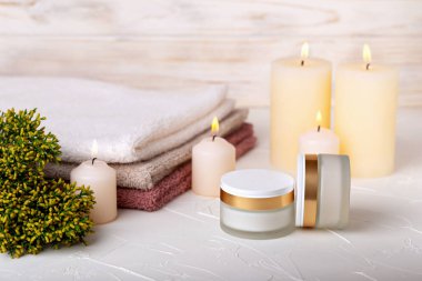 Yüz kremli iki kavanoz, yanan mumlar, havlular ve arka planda ardıç dalı. Sakinlik, rahatlık, spa tedavisi kavramı. Seçici odak