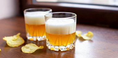 İki bardak taze, filtresiz bira ve patates cipsi, ahşap pencere eşiğinde.