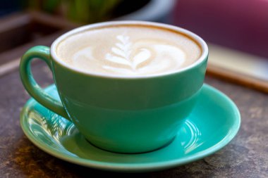 Masanın üzerinde yeşil seramik bardakta desenli taze aromatik kahve lattesi. Nefis bir kahvaltı. Seçici odak