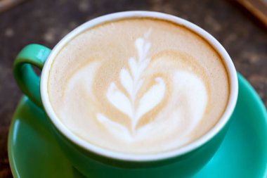 Taze aromalı latte köpüklü ve yeşil bardakta yakın plan kahve. Nefis bir kahvaltı. Seçici odak