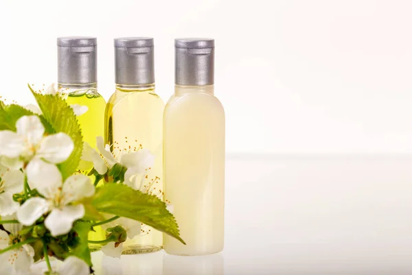Three small bottles of cosmetics and flowers with leaves on white background. Shampoo, shower gel, body lotion. Travels, trips, hotels. Natural organic cosmetics