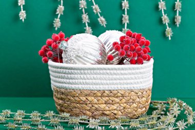 Noel süslemeleri katmanları ve donmuş kırmızı rowan sepeti içinde yeşil arka planda. Her taraf ışıl ışıl çelenkler. İyi tatiller.