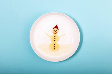 Peynirden, pancar kökünden ve mavi arka planda beyaz tabakta biberden yapılmış güzel bir kardan adam figürü. Yemeklerden yapılmış şenlikli dekorasyonlar.