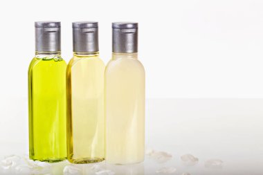 Hafif arka planda beyaz yapraklı kozmetik ürünleri olan üç küçük şişe. Şampuan, duş jeli, vücut losyonu. Seyahatler, turizm, oteller. Doğal organik kozmetik. Vücut bakımı
