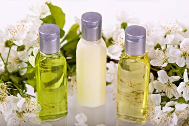 Taze beyaz çiçekler arasında üç şişe kozmetik, cilt bakımındaki doğal güzelliğin somutlaşmış özü. Şampuan, duş jeli, vücut losyonu. Seyahatler, geziler, oteller. Doğal organik kozmetik