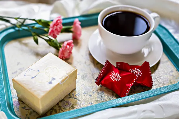 Romantik kahvaltı. Süslü kahvaltı tepsisi, bir fincan sade kahve, kırmızı paket çikolata, hediye kutusu ve pembe çiçekler. Özel günler ve romantik sabahlar için mükemmel. Sevgililer Günü