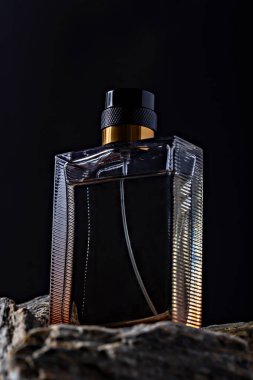 Şatafatlı siyah parfüm şişesi, desenli tasarım, altın aksanlarla vurgulanmış, kayalık yüzeyde koyu arkaplan üzerine yerleştirilmiş. Reklam ve ürün sunumları için mükemmel.