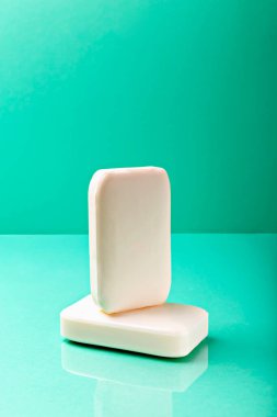 Yansıtıcı ve canlı turkuaz yüzeydeki iki beyaz sabunun temiz kavramsal görüntüsü tazeliği, hijyeni ve minimalist stili sembolize ediyor.