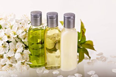 Beyaz arka planda beyaz kiraz çiçekleriyle çevrili doğal yağlarla dolu üç şişe. Temizlik, sağlık ve doğal güzellik kavramları. Spa, sağlık ve cilt bakım konuları için ideal