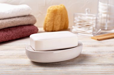 Etrafı havlularla ve ahşap arka planda kaplıca aksesuarlarıyla çevrili, sabun tabaklarında dinlenen beyaz sabun. Hijyen, temizlik, rahatlama, kaplıca ve kendine bakım kavramını. Sabun ve aksesuarlı banyo.