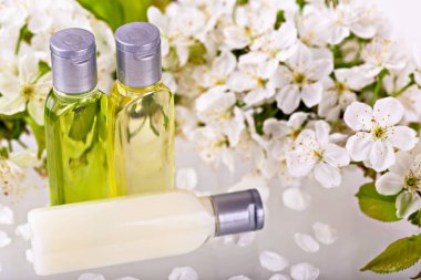 Hassas beyaz çiçeklerin arasına yansıtıcı bir yüzeye yerleştirilmiş gümüş kapaklı üç organik deri şişesi. Doğal yağlar ve losyonlar saflık ve sağlık iletir. Güzellik, kaplıca ve kendine özen kavramı