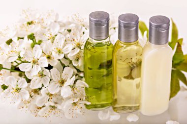 Yumuşak arka planda beyaz kiraz çiçeklerinin arasına yerleştirilmiş gümüş kapaklı üç deri şişesi. Doğal yağlar ve losyon organik güzellik ve sağlığın altını çizer. Spa, kişisel bakım ve aromaterapi kavramı