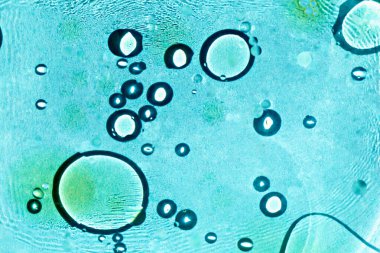 Soyut mavi sıvı kabarcıklar farklı boyutlarda ve şeffaflıkla dinamik bileşim oluştururlar. Işık sıvıda kırılır. Yağ suyun üstünde daireler çizer. Yaratıcı tasarımlar için arka plan. Seçmeli odak, ayrışma